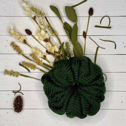 Green hand knit jumbo scrunchie on a white wooden surface with floral elements